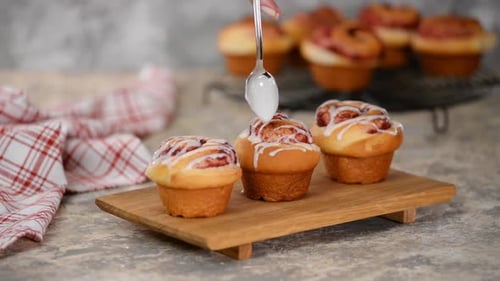 Pouring icing over swirl buns with jam.