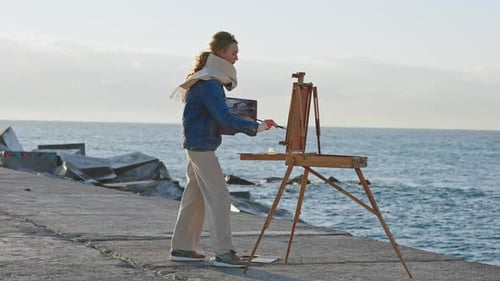 Woman Painting on Shore Next to Easel
