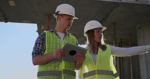 Two Engineers a Man and a Woman with a Tablet Computer at a Construction Site Condemn the