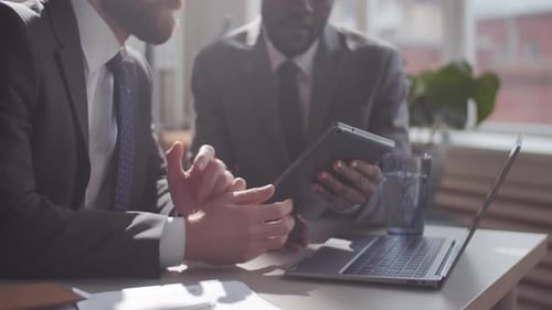 Two Multiethnic Business Partners Using Tablet and Talking at Office Desk