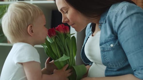 Blonde Infant Giving Tulips to Adult Indoors