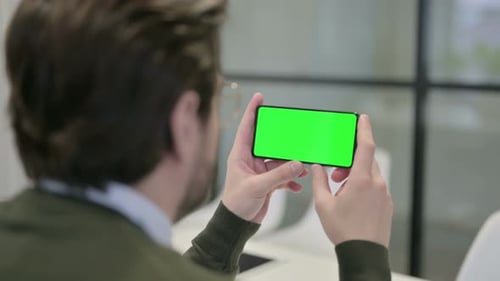 Young Adult Holding Smartphone with Green Screen in Office