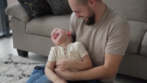 Happy Father Tickling Laughing Son on Rug Indoors