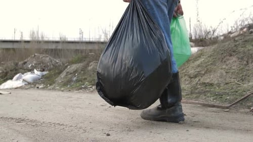 Person Carries Trash Bags Through Polluted Urban Area
