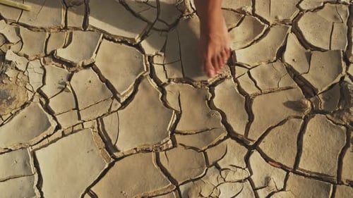 Top view of barefoot feet stepping on a dry broken ground.