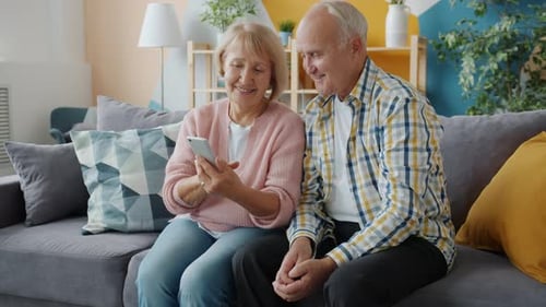 Smiling Senior Couple Using Smartphone on Couch