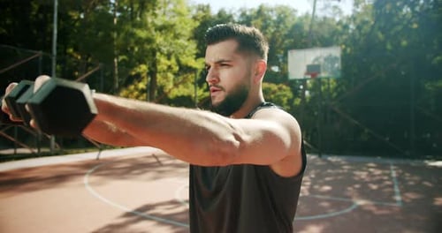 Sporty Man Lifting Weights with Both Hands in a Public Park Dumbbell Training