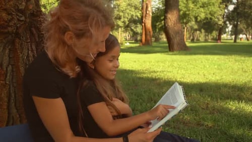 Mother and Daughter Reading Book Under a Tree