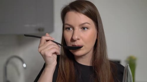 Woman Tastes Food with Spoon in Kitchen