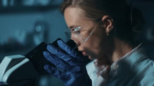 Woman Scientist Looking Through Microscope in Dark Lab