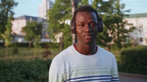 A Young Black Student with Headphones Walks Through the City Centre at Sunset