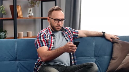 Man Relaxing on Couch Using Mobile Phone