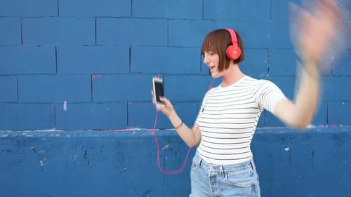 Woman Dancing with Headphones Against Blue Brick Wall