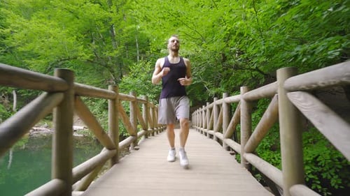 Man Running Across Wooden Bridge in Forest
