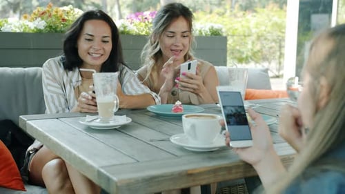 Joyful Girls Friends Looking at Smartphone Screen Swiping Having Fun in Cafe Enjoying Content