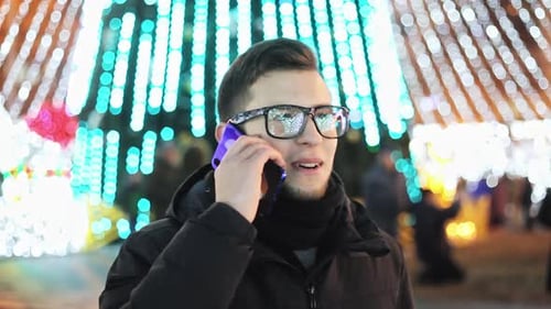 Stylish Man Talking on the Phone on Christmas Night on the Street Decorated with Festoons