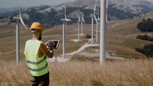 Adult engineers in yellow hard hat and green uniform checking the wind turbine system