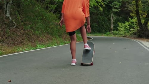 Skateboarder Girl is Riding Skateboard Outdoor in Park Rolling Over Road Rear View