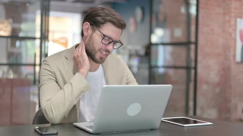 Man Using Laptop and Rubbing Neck at Desk