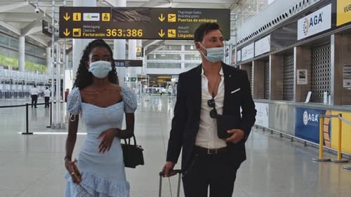 Man with Luggage with Woman As They Both Wear Masks and Airport Terminal