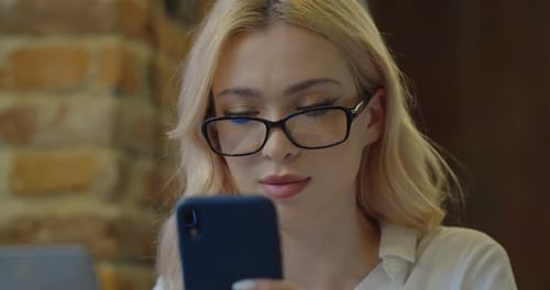 Beautiful Businesswoman Sitting in Cafe and Texting on Smartphone