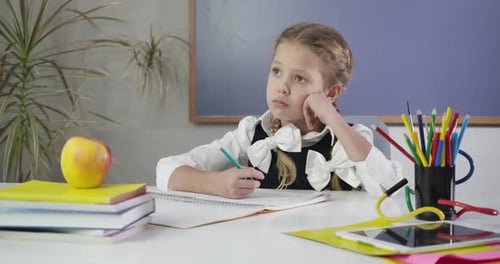 Portrait d'une jolie fille caucasienne assise, écrivant dans un cahier d'exercices et regardant ailleurs pensivement