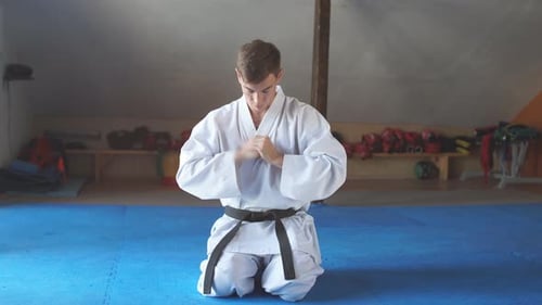 Karate Man in Kimono Sits on Knees on Floor in Martial Arts Gym