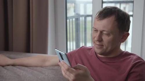 Man Uses Smartphone While Relaxing on Couch