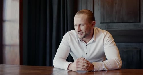 Geschickter männlicher Unternehmer schaut weg und lächelt, während er am Tisch sitzt und über Tricky nachdenkt