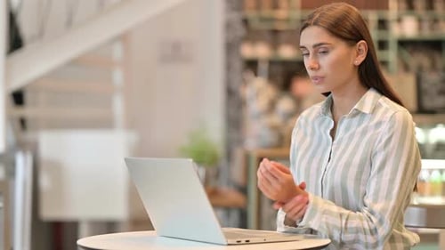 Young Latin Woman with Laptop Having Wrist Pain in Cafe
