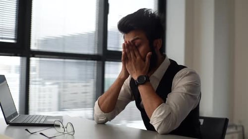 Stressed Young Adult Rubbing Face at Office Desk