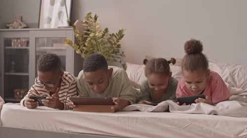 Four Children Using Technology on a Bed
