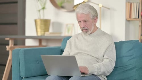 Worried Senior Man Uses Laptop in Living Room