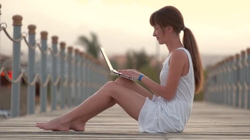 Junge Frau surft an einem warmen Sommerabend draußen im Internet auf einem Laptop
