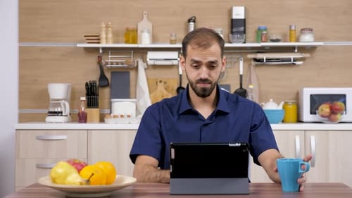 Man using Tablet in Kitchen Drinking from Mug