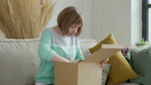 Woman Unpacking a Box on Couch in Home