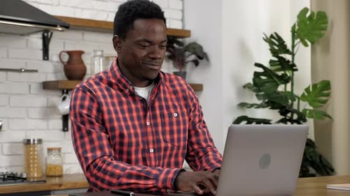 Man Smiling and Typing on Laptop in Kitchen