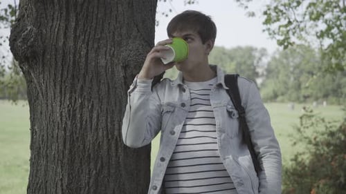 Young Man Drinking Coffee in a Green Park