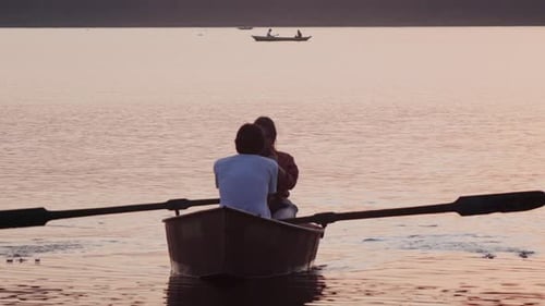 Couple Rowing Boat on Peaceful Lake at Sunset