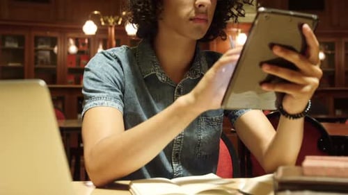 Young Adult Uses Tablet in Library Setting