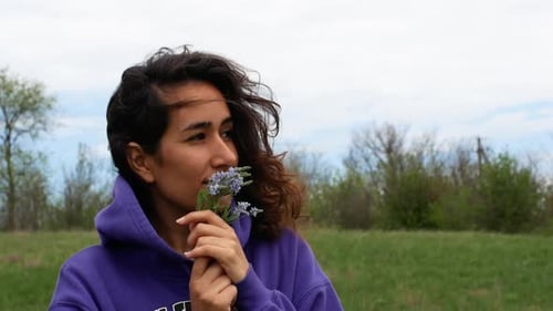 A beautiful woman holds field spring flowers in her hands. The girl in the field admires the flowers