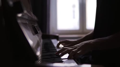 Man Plays Piano Keys in Dimly Lit Room