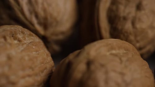 Cinematic, rotating shot of walnuts in their shells on a white surface