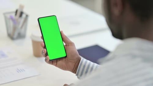 Rückansicht eines afrikanischen Mannes, der Videoanrufe auf einem Smartphone mit Chroma-Bildschirm tätigt