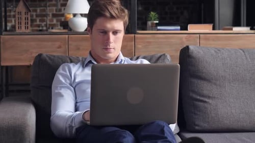Man Works on Laptop While Relaxing on Couch