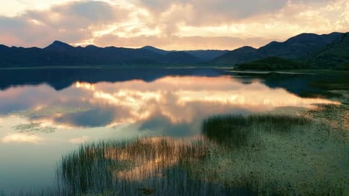 Beautiful sunset sky reflected in lake - marsh grass and silhouettes of mountains