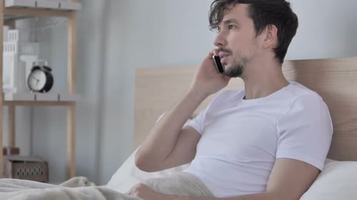 Homme parlant au téléphone alors qu'il est allongé sur le côté dans son lit