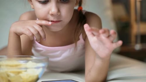 Girl Uses Phone and Eats Chips in Bedroom