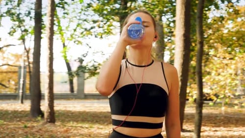 Woman Drinks Water During Autumn Workout in Park