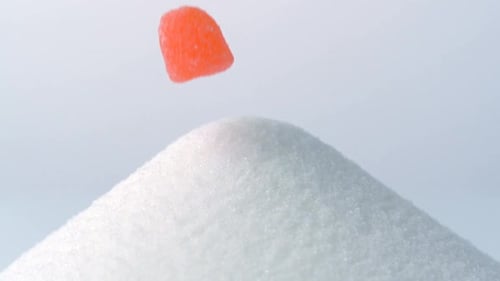 Gummy Candies Falling onto Pile of White Sugar